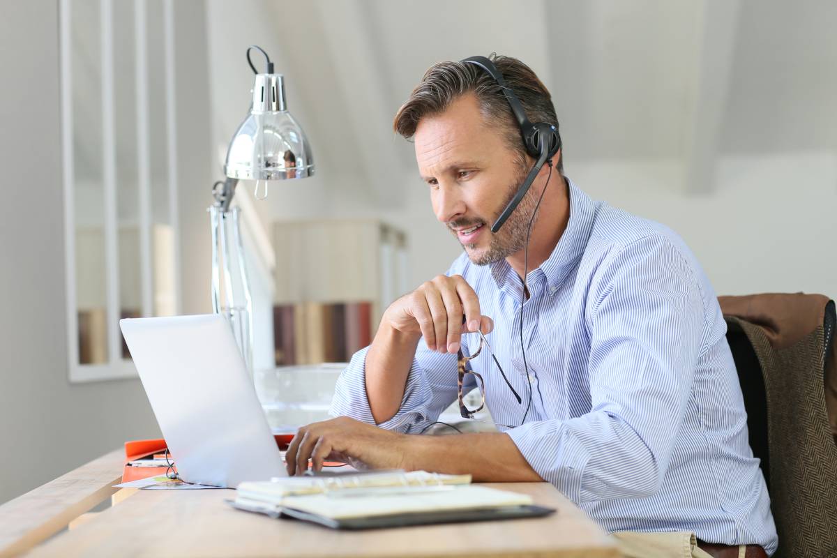 A man working from home using a laptop and a headset and providing great customer service
