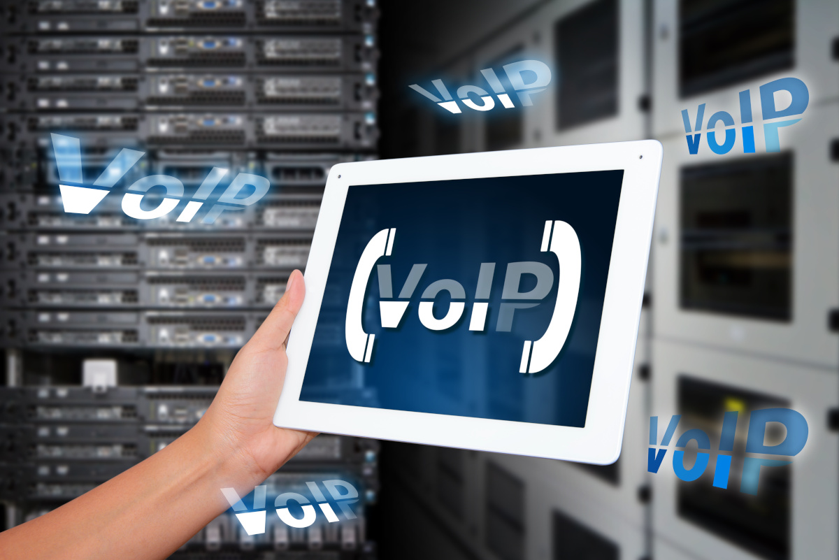 Hand Holding Tablet with VoIP Lettering on Server Room Background