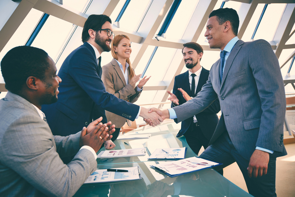 Two Businessmen Shaking Hands with Three Colleagues Applauding