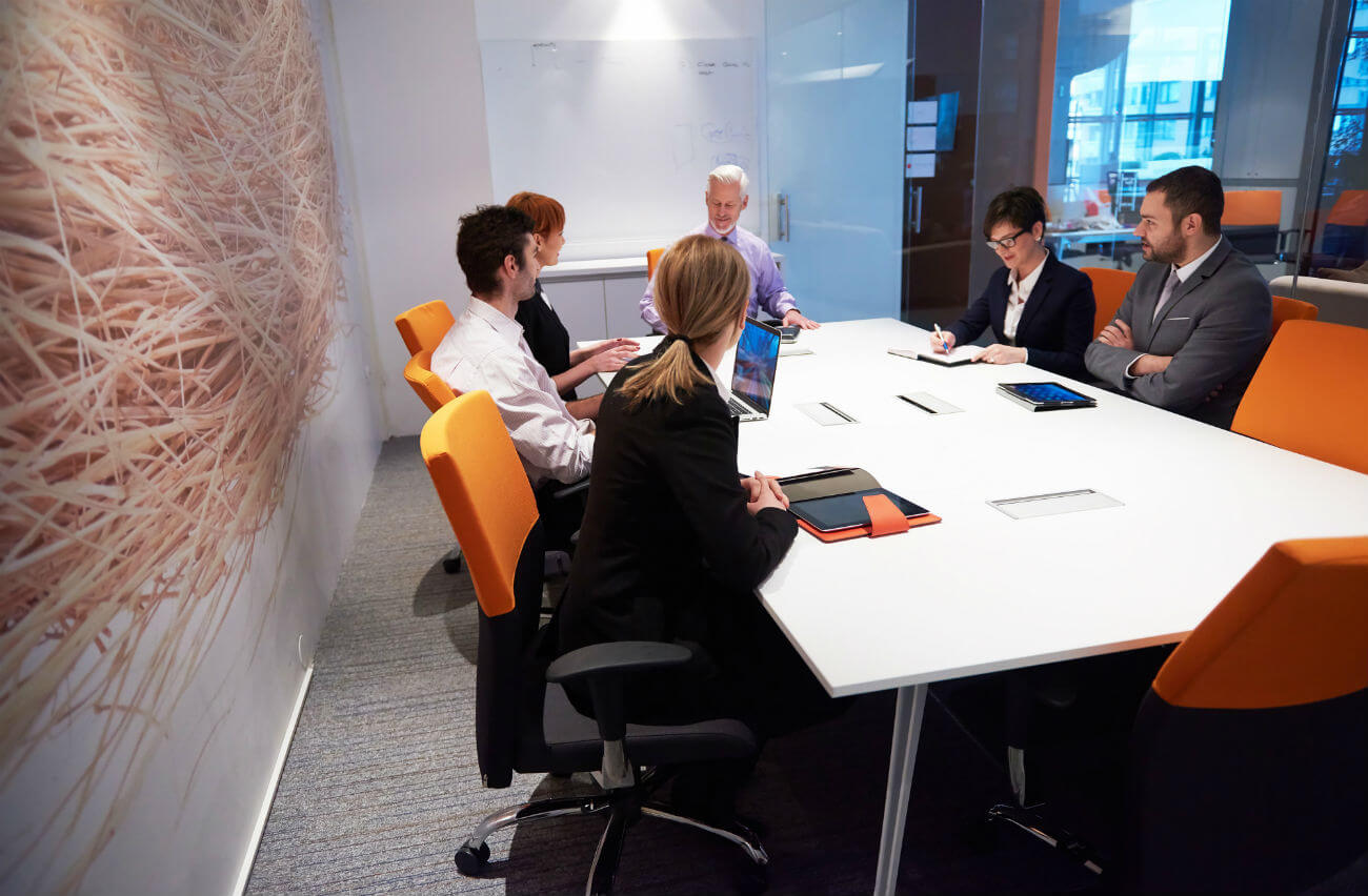 Businessman and businesswomen sitting at a conference table in orange chairs